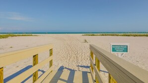 Un muelle de madera que lleva a una playa, con un cartel que indica 'Sandpiper Beach Condominium Private'.