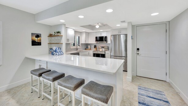Una cocina moderna con una isla grande, taburetes de bar, electrodomésticos de acero inoxidable y un ventilador de techo.