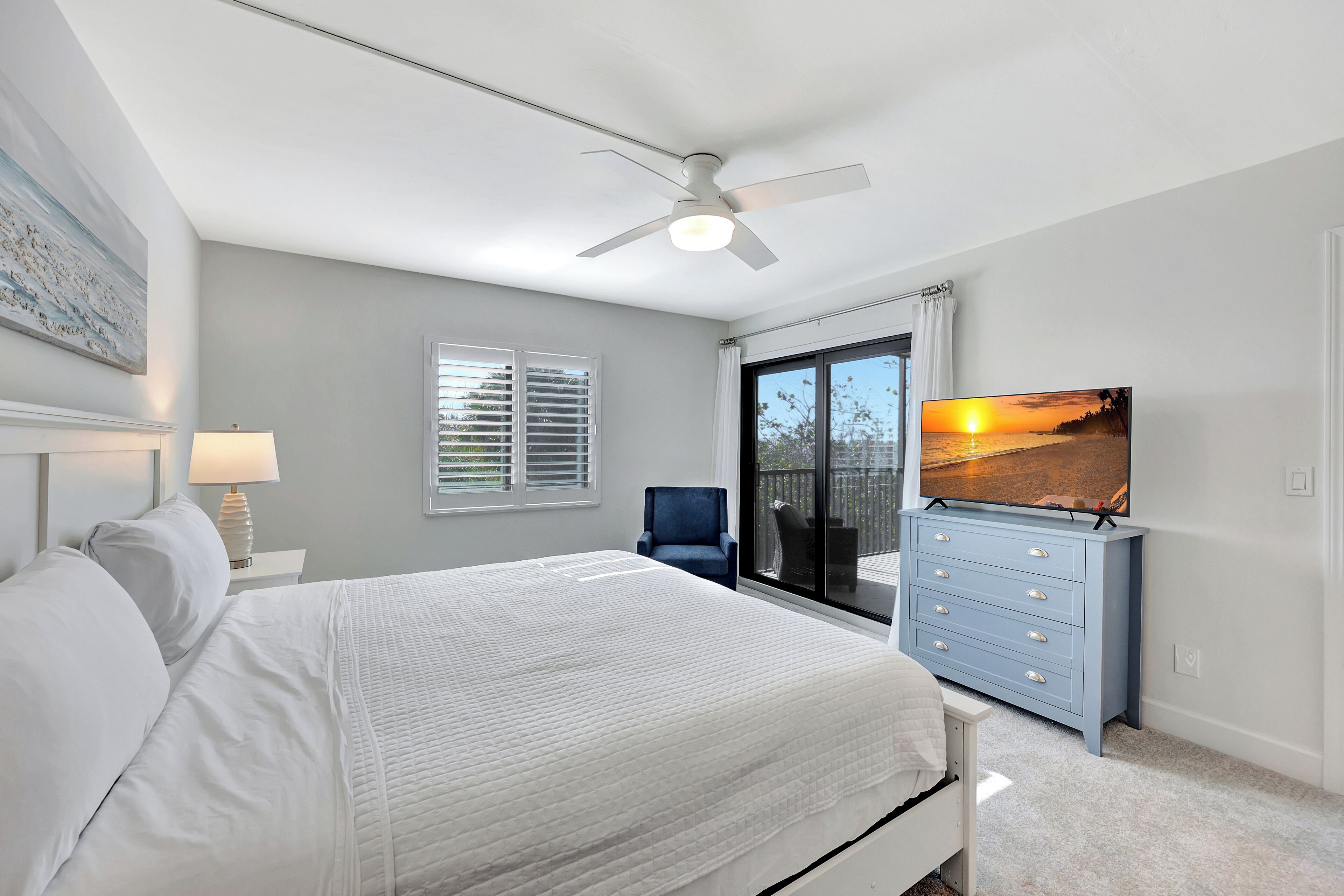 A bedroom with a bed, a ceiling fan, a TV on a dresser, a chair, and a window with blinds.