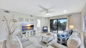 Una sala de estar moderna con un televisor de pantalla plana, sofás grises, una mesa de centro y un ventilador de techo.