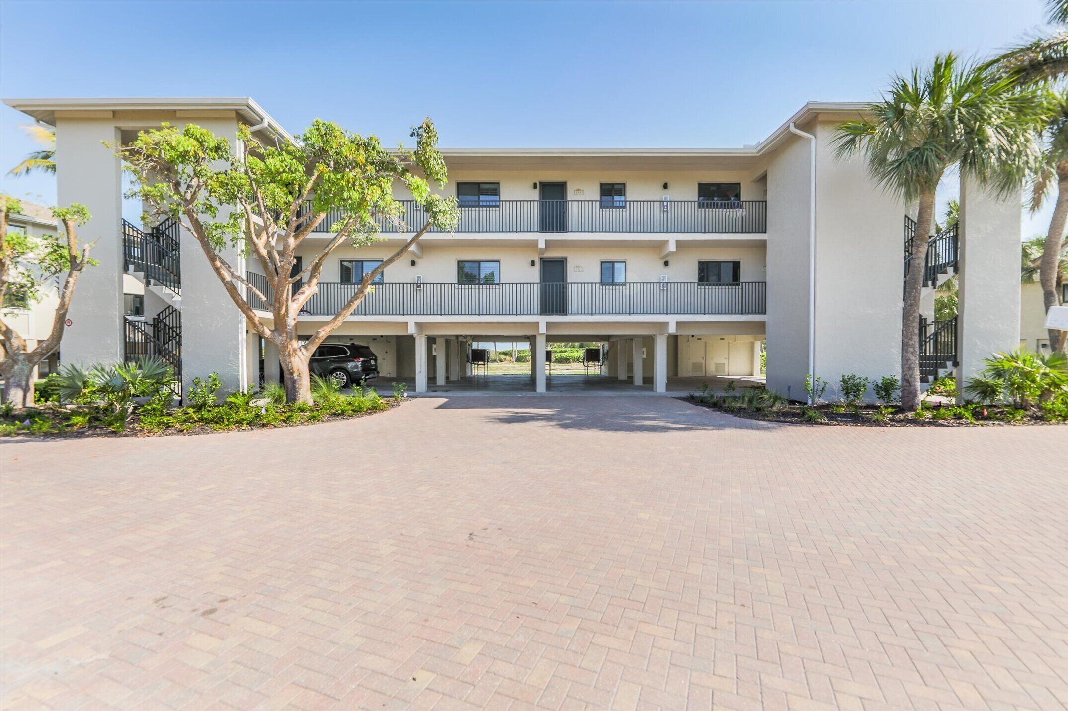 A multi-story residential building with balconies, a paved driveway, and surrounding greenery.