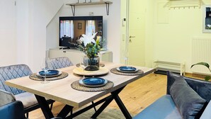 A modern dining area with a wooden table set for four, a sofa, and a television in the background. - Modern vacation apartment in Anklam - right next to the city center (Anklam)