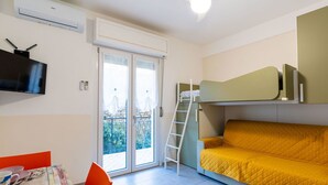 Habitación compacta con literas, una mesa con sillas, un televisor y un ventilador de techo.