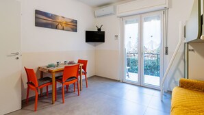 Un espacio habitable compacto con comedor, televisor montado en la pared y balcón con vistas.