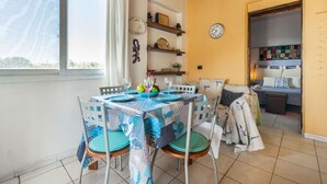 A dining area with a table set for two, chairs with green cushions, a clock on the wall, and a view of the outside through a window. - Beautiful apartment in villa for 4 guests with WIFI, A/C, TV, patio, pets allowed and panoramic ... (Muravera)
