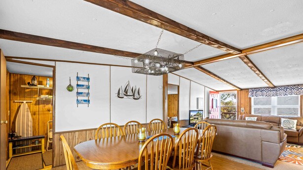 Un comedor amplio con una mesa y sillas de madera, una araña, y una sala de estar acogedora con un sofá y un tapiz estampado.