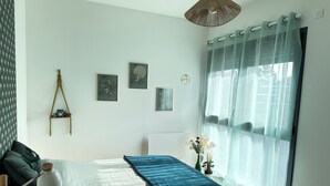 Ein Schlafzimmer mit Bett, Nachttisch, Lampe, Fenster mit leichtem Vorhang und Wandbild.