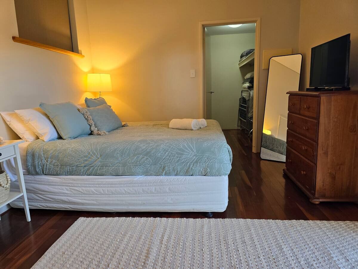 Quarto com cama, mesa de cabeceira, abajur, cômoda e televisão.
