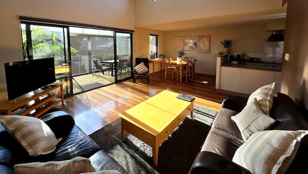 A spacious living area with a sofa, a coffee table, and a TV. There is a sliding glass door leading to a balcony.