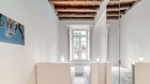 A narrow, well-lit room with a wooden ceiling, a large window, and a bed with a bedside table. - Pleasant Family Apt next to Lake Como (Como)