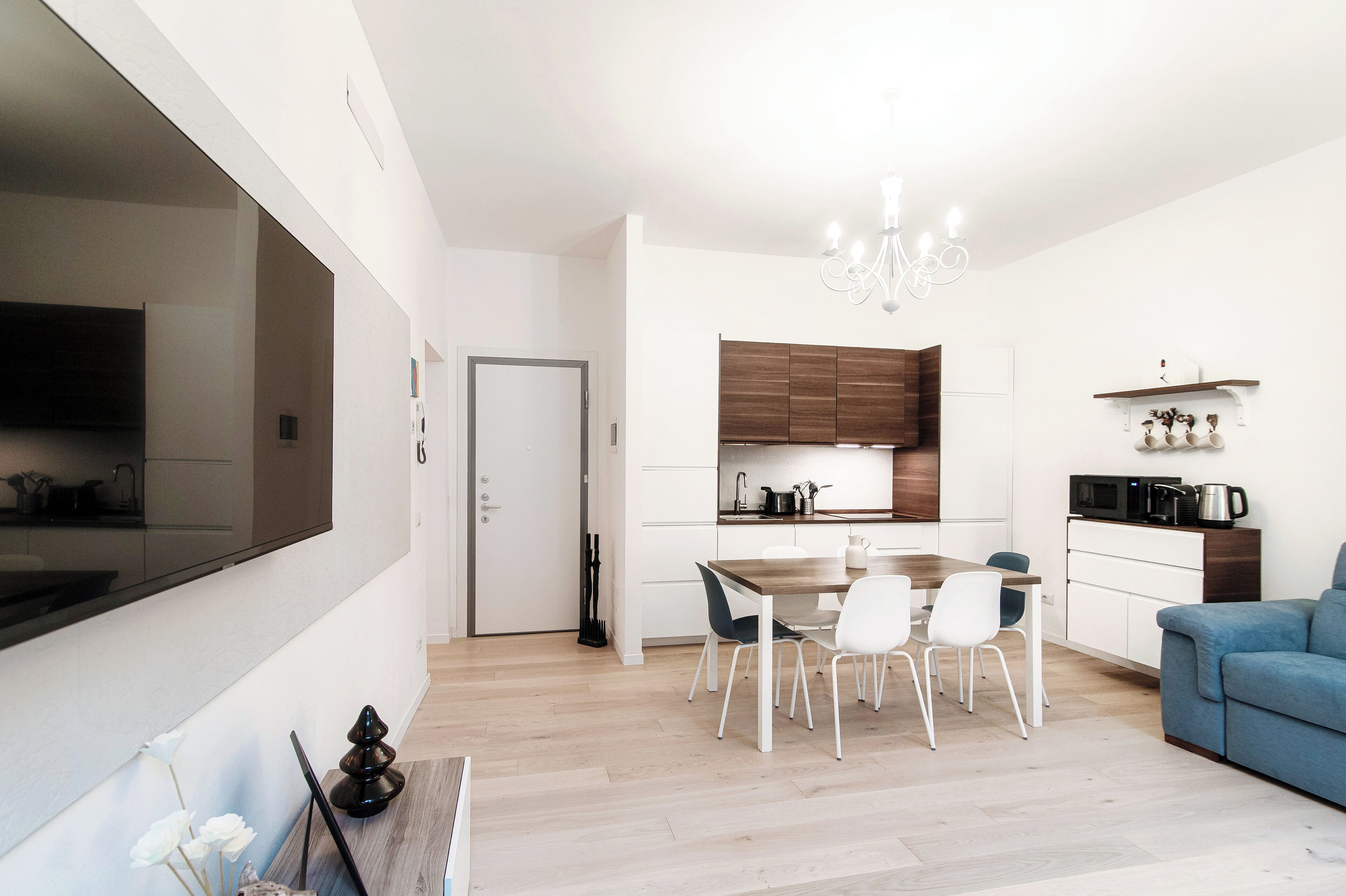 A modern kitchen with white cabinets, a wooden dining table, and a blue sofa in the living area.