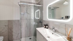 A modern bathroom with a glass-enclosed shower, a large mirror with integrated lighting, and a white sink with a single faucet. - Pleasant Family Apt next to Lake Como (Como)