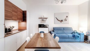 Una cucina moderna con mobili bianchi, un tavolo da pranzo in legno e un divano blu in zona living.