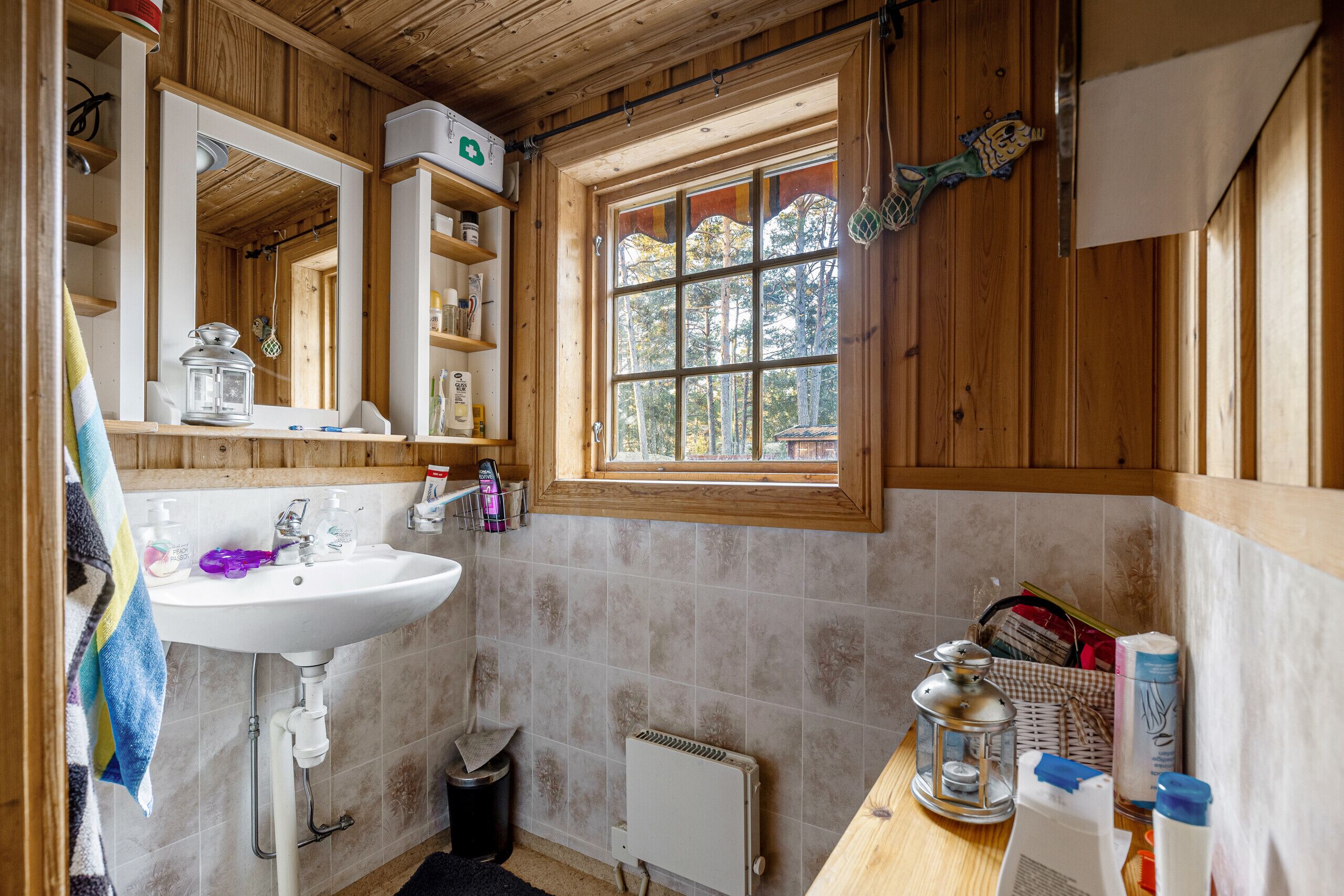 Ein Badezimmer in einer Holzhütte mit Waschbecken, einem Fenster mit Blick auf Bäume und einer kleinen Mülleimer.