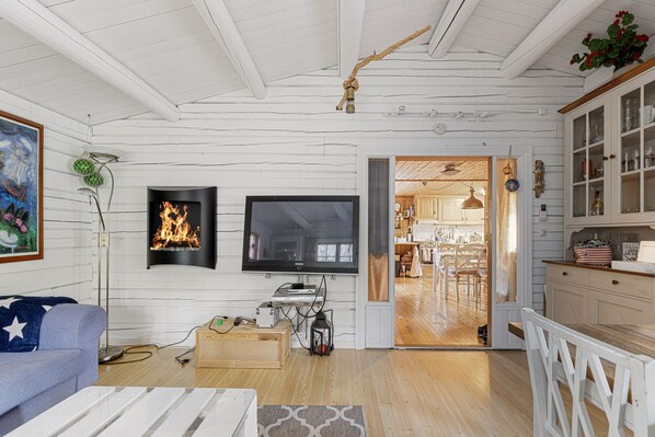A living room with a fireplace, a television, and a wooden dining area visible through an open door.