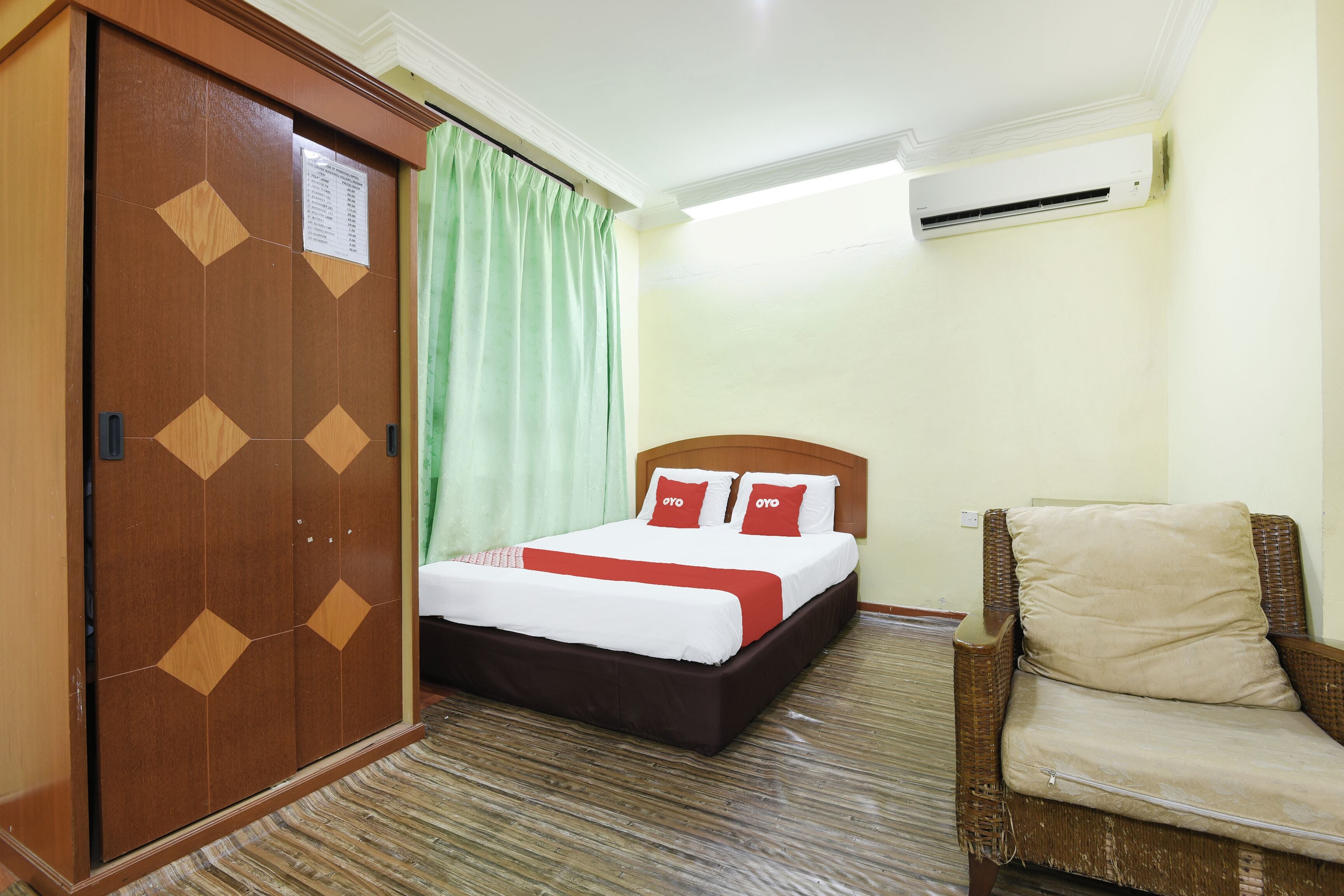 A hotel room with a bed, a chair, a wardrobe, and an air conditioning unit.