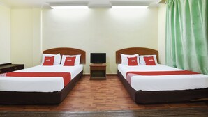 A hotel room with two beds, each with white bedding and red pillows, a small bedside table with a TV, and a green curtain on the window.