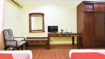 Quarto de hotel com duas camas, uma escrivaninha de madeira com televisão, uma cadeira e um guarda-roupa.