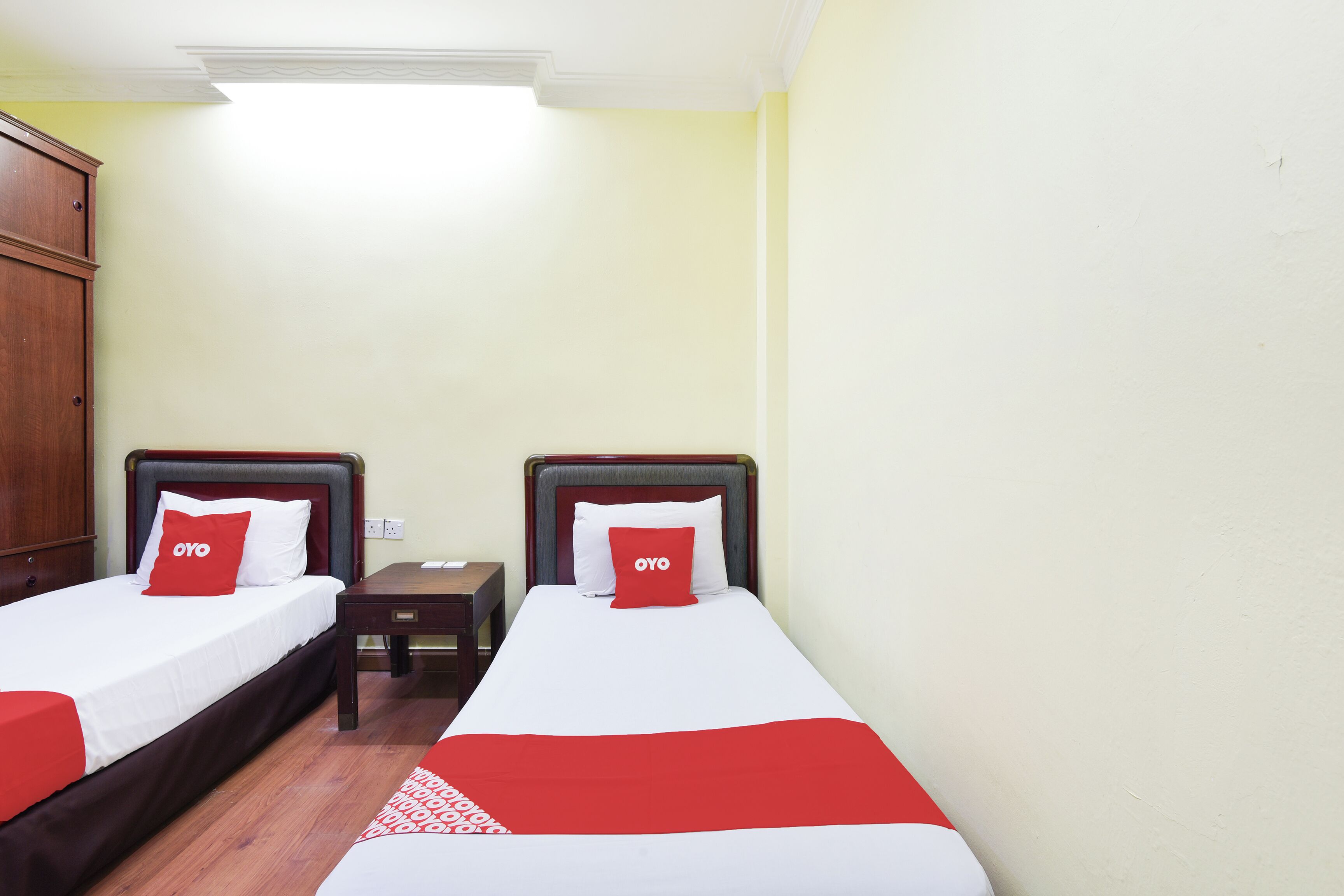 A hotel room with two single beds, each with a red and white bedspread and matching pillows.