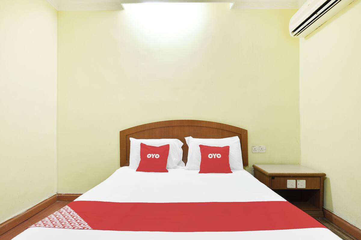 A neatly made bed with two red pillows, a wooden headboard, and a bedside table with a lamp.