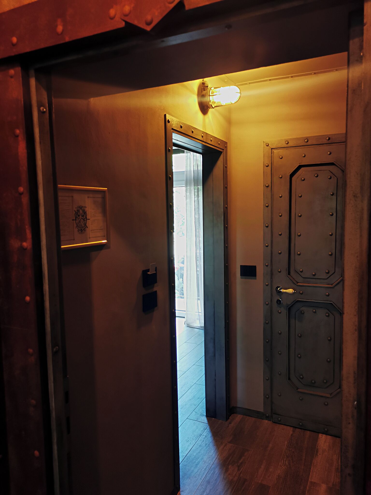 A narrow hallway with a wooden door on the right, a light fixture above it, and a door with a brass handle.
