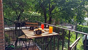 Um deck de madeira com uma mesa posta para o café da manhã, incluindo croissants, xícaras de café e um copo de suco de laranja.
