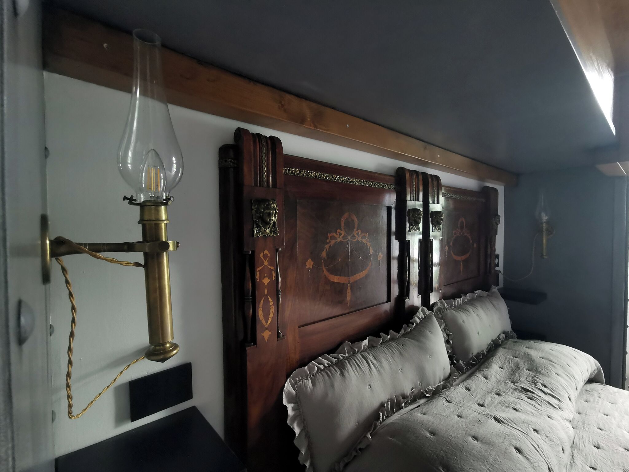 A bedroom with a wooden headboard, a brass lamp, and a bed with ruffled pillows.