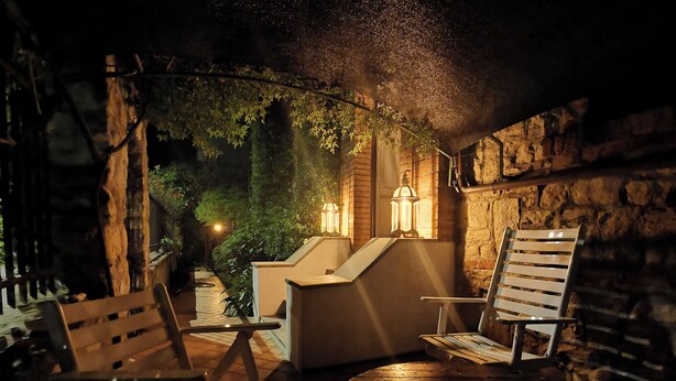 An outdoor seating area with wooden chairs and a table, surrounded by stone walls and greenery. - The Kraken Inn (Bergamo)