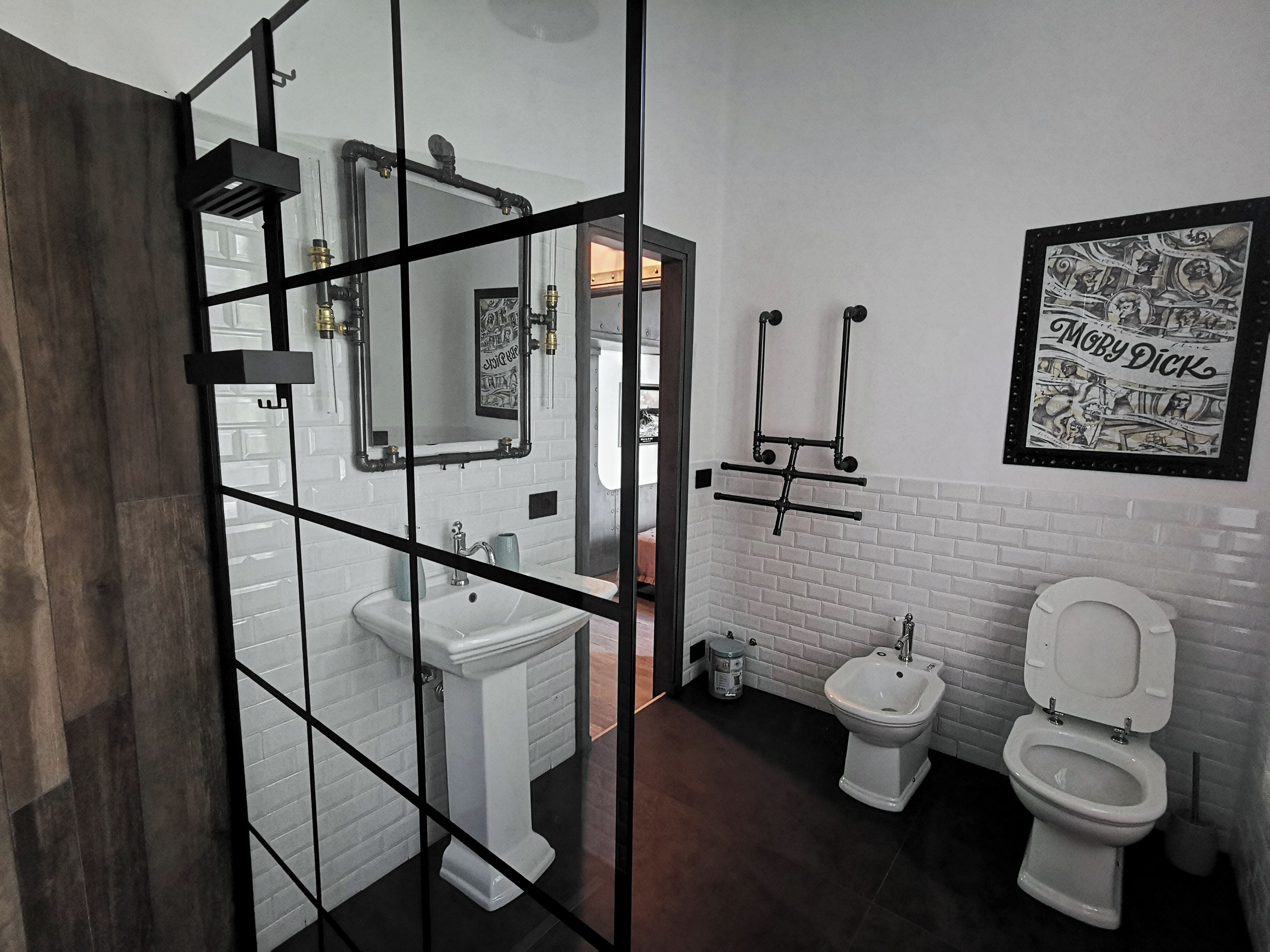 A modern bathroom with a white sink, a bidet, and a toilet. There is a mirror with a black frame, and a picture of 'Moby Dick' on the wall.