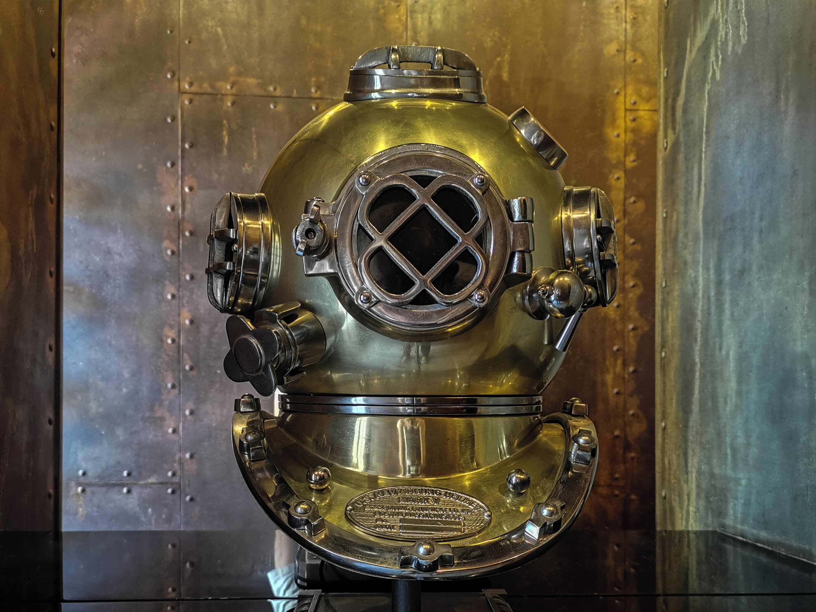A vintage diving helmet with a circular window and ventilation holes, mounted on a stand.