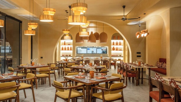 A spacious dining area with multiple tables and chairs, warm lighting, and a large TV screen in the background. - Mharo Khet (Jodhpur)