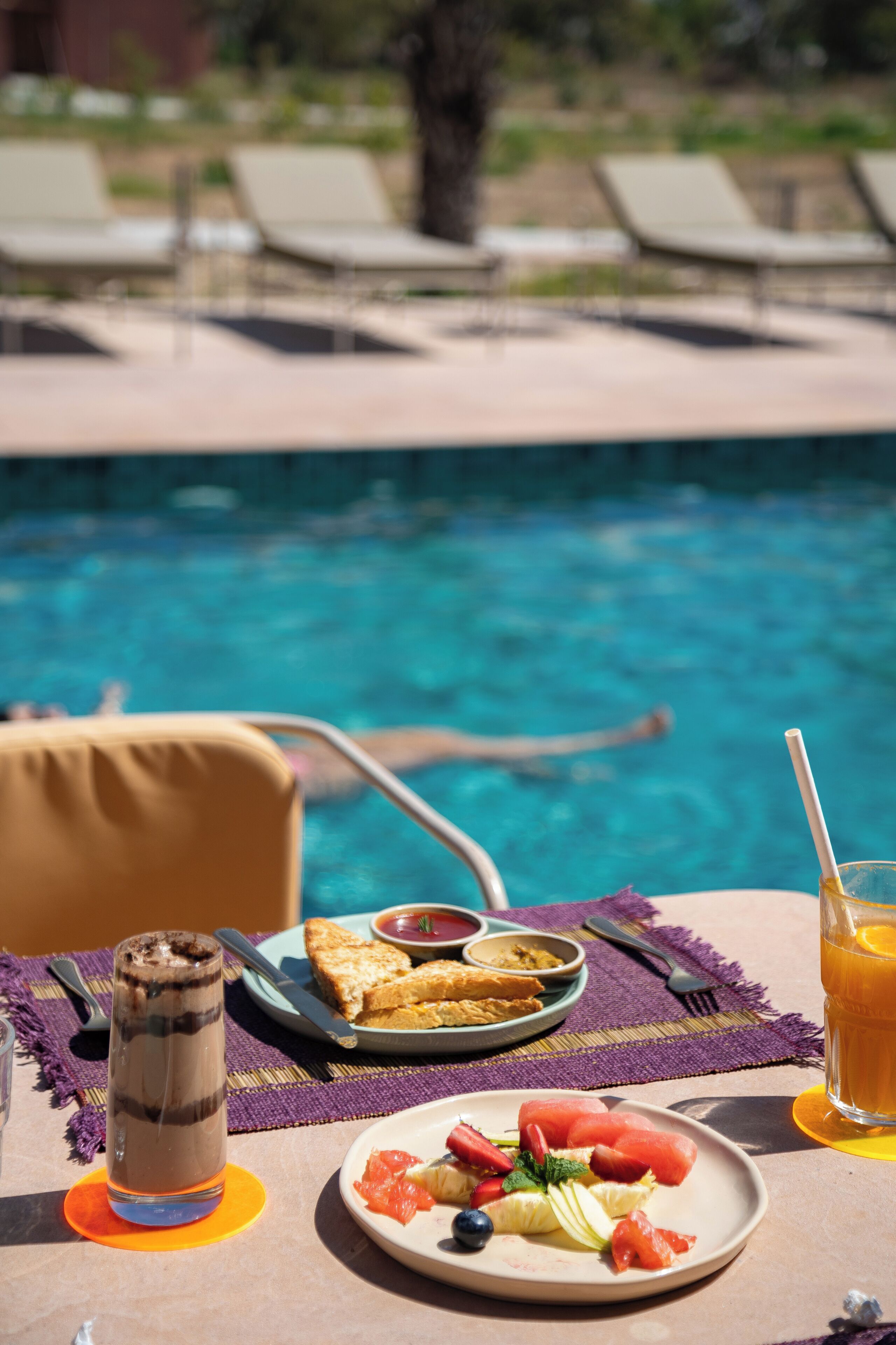 A dining table with breakfast items, a glass of orange juice, and a poolside view.
