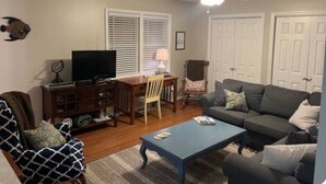A living room with a television, a coffee table, a sofa, a chair, and a ceiling fan.