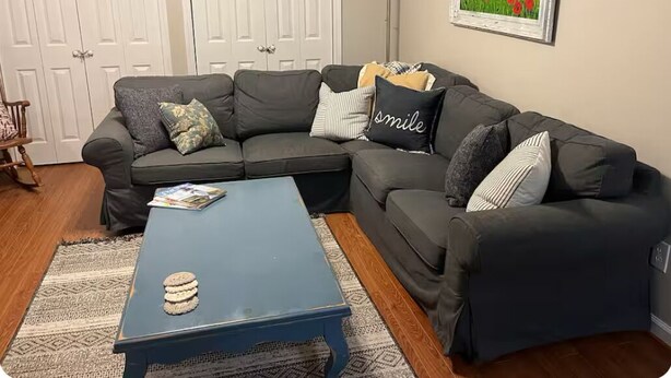 A living room with a dark gray sectional sofa, a blue coffee table, and a framed landscape painting on the wall.