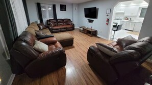 A living room with a brown leather sofa, a flat-screen TV, and a kitchen visible through an open doorway. - Welcome to Kozykave (Kawartha Lakes)