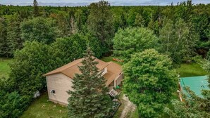 A single-story house surrounded by dense forest. - Welcome to Kozykave (Kawartha Lakes)