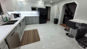 A modern kitchen with white cabinets, a black refrigerator, and a dining area with a black chair. - Welcome to Kozykave (Kawartha Lakes)