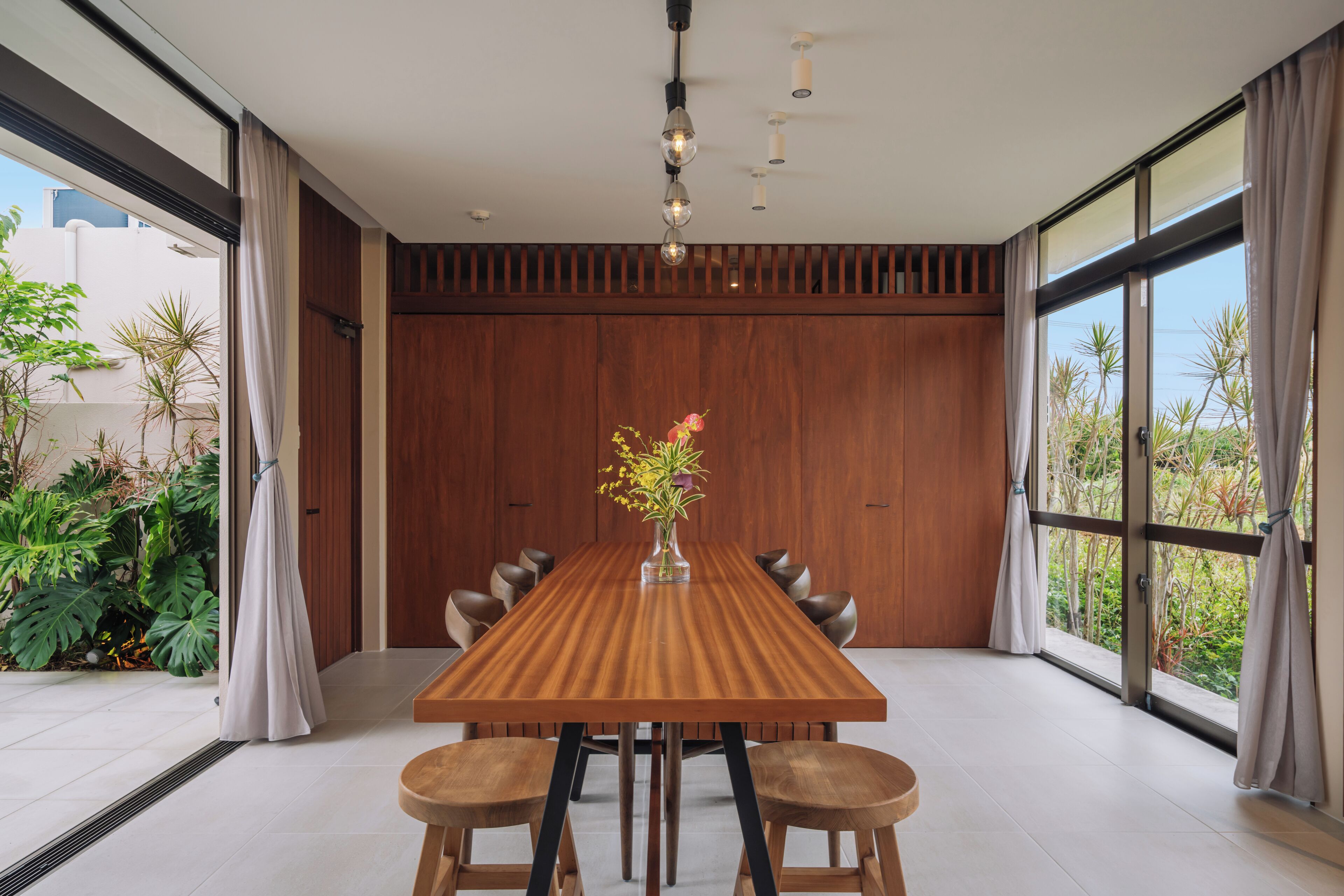 A modern dining area with a wooden table, six chairs, and a vase with flowers.