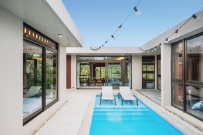 A modern outdoor pool area with glass doors, a seating area, and string lights. - Reflexion Villas GLANZ (Nago)