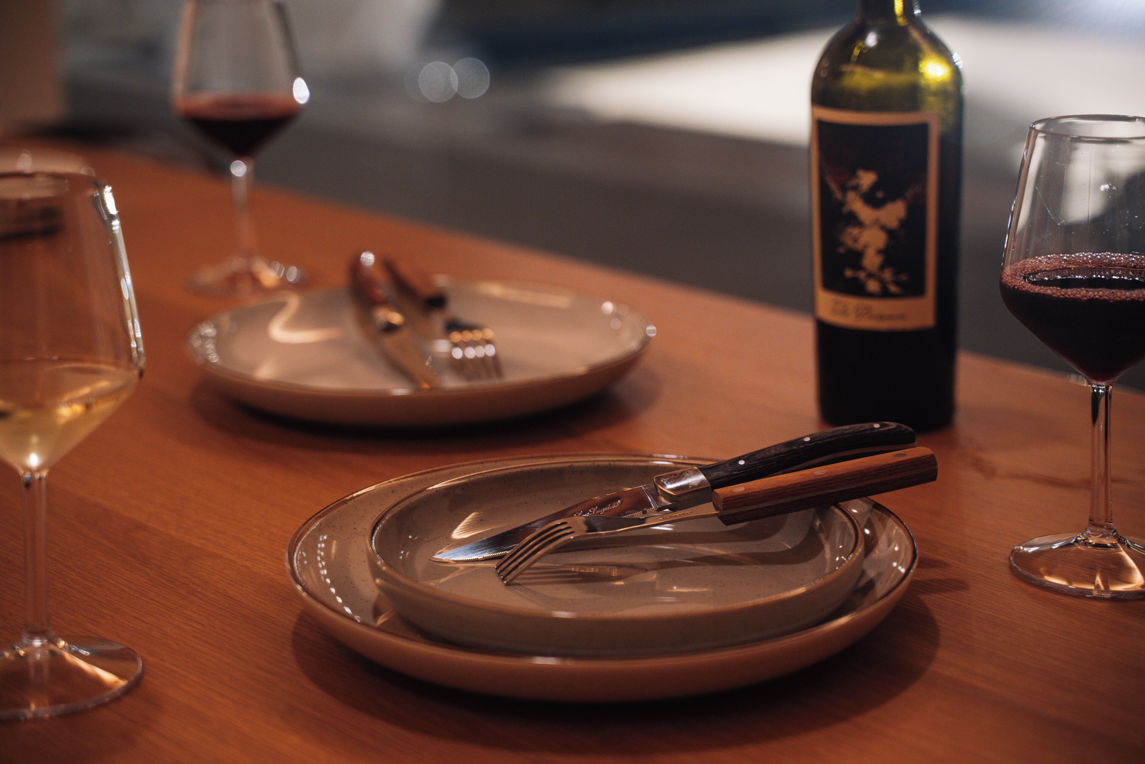 A dining table with plates, cutlery, and wine glasses.