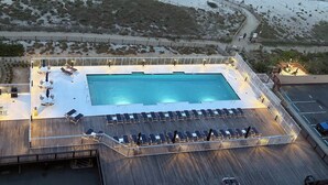 Een luchtendakfoto van een resort met een zwembad, ligbedden en een strandgedeelte.