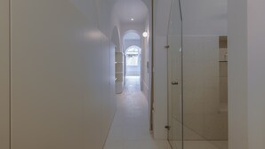 A narrow, well-lit hallway with white walls and a tiled floor, leading to a bright room with a large window. - Alameda Terrace by Homing (Lisbon)