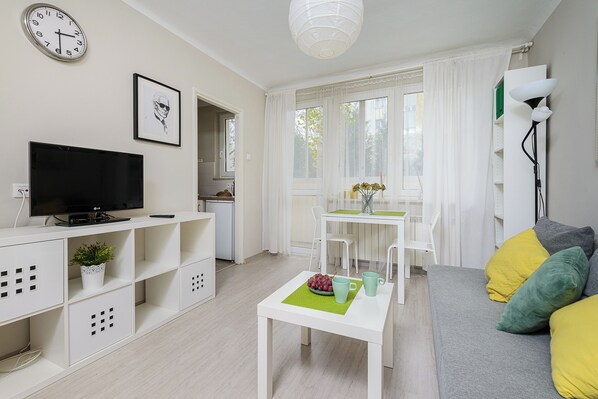 A modern living room with a flat-screen TV, a dining area with a table and chairs, and a sofa with cushions.