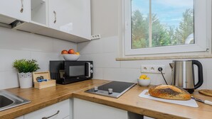 Una cocina con armarios blancos, un microondas, una tetera y una barra de pan sobre el mostrador.