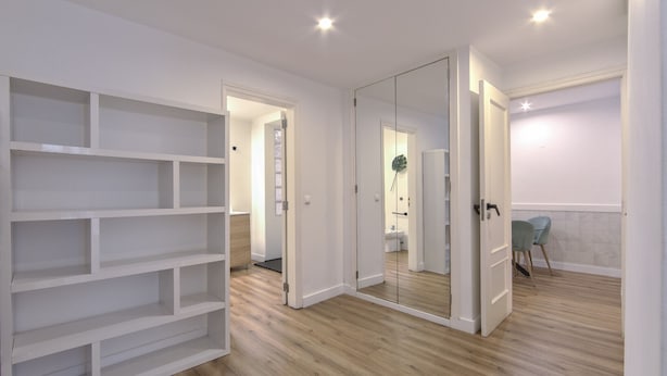 A spacious room with a wooden floor, a white shelving unit, and a large mirror. - Bairro Alto Design by Homing (Lisbon)