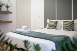 Un lit bien fait, avec une couverture verte, des oreillers blancs et un coussin assorti posé sur la tête de lit.