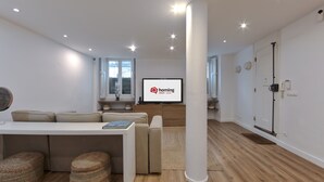 A modern living room with a sofa, ottomans, a coffee table, a flat-screen TV, and a large pillar. - Bairro Alto Design by Homing (Lisbon)