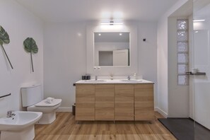 Une salle de bain moderne avec un meuble-lavabo en bois, deux vasques, des toilettes et un bidet.