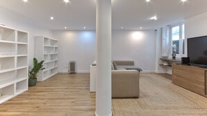 A modern living room with a large white column, built-in shelving, a sofa, a television, and a radiator. - Bairro Alto Design by Homing (Lisbon)