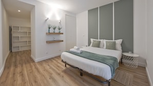 A modern bedroom with a bed, bedside tables, a shelf with plants, and a wardrobe. - Bairro Alto Design by Homing (Lisbon)